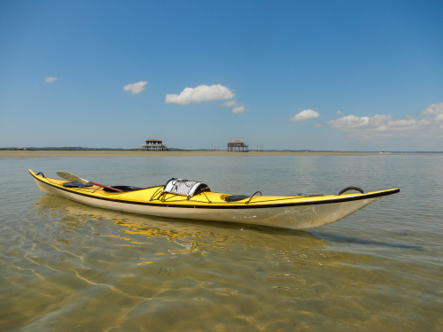 un kayak de mer jaune, sur l'eau devant les cabanes tchanqu&eacute;es du bassin d'Arcachon