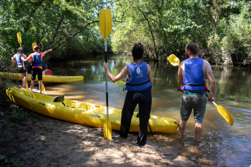 4 personnes se tiennent &agrave; c&ocirc;t&eacute; de cano&euml;-kayak jaunes au bord de la Leyre.