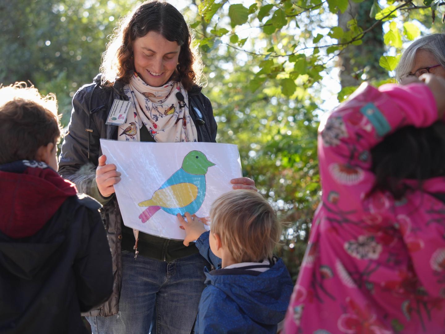Une animatrice naturaliste présente un dessin d'oiseau à un groupe d'enfant.
