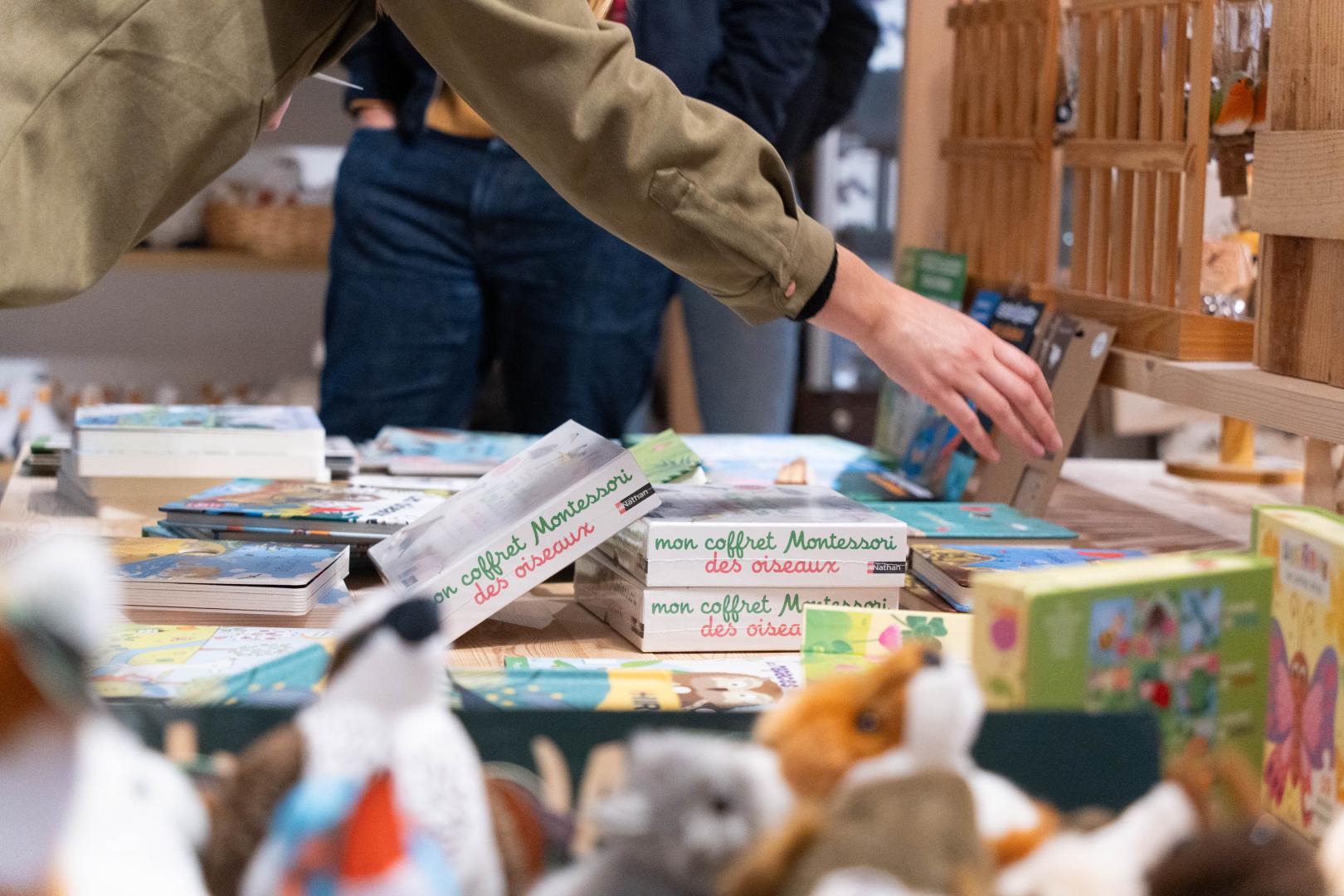 Un visiteur attrape un livre sur une étagère remplie de livres pour enfant et de jeux à la boutique de l'oiseau.